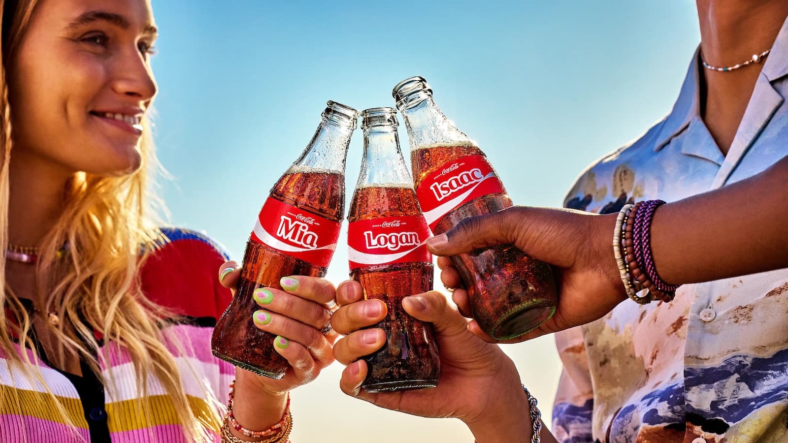 An image from Coca-Cola's Share a Coke campaign of three people tapping their Coke bottles together.