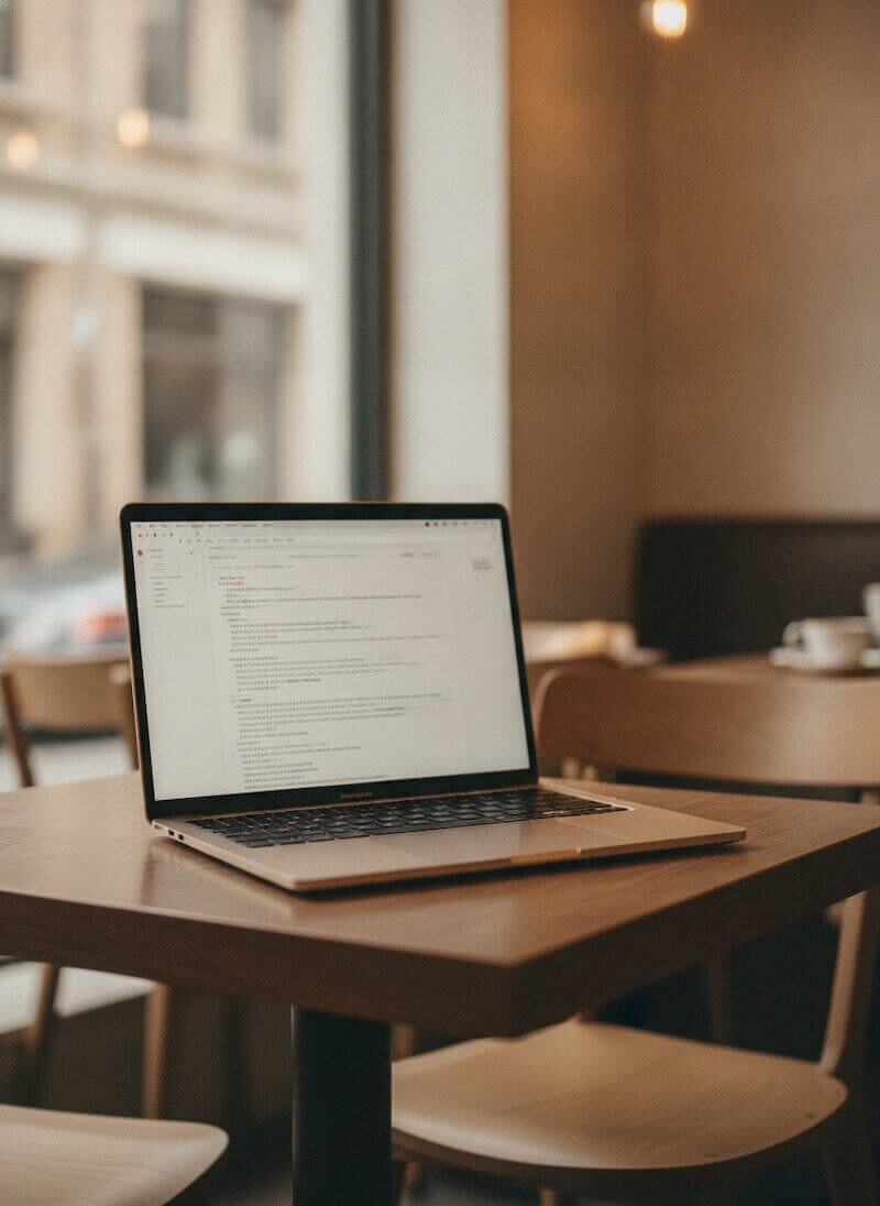 Laptop on a cafe table with English text on screen, warm coffee shop atmosphere.