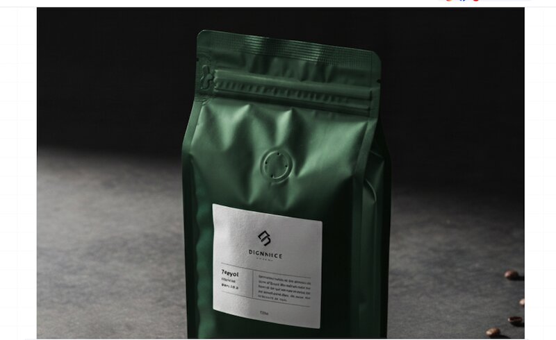 Green matte coffee bag on a concrete surface with scattered beans and a white minimalist label, dark background.