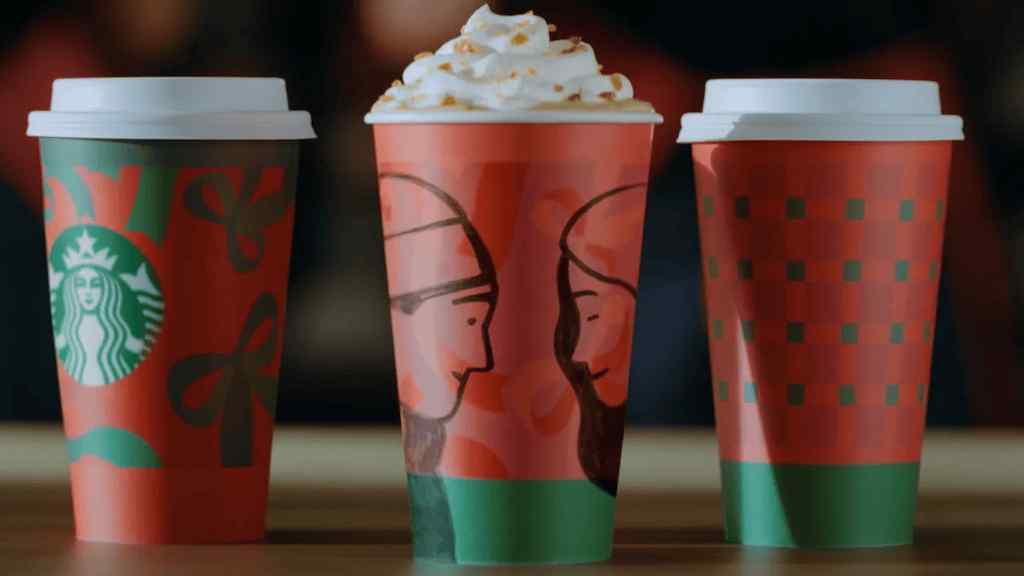 Three festive Starbucks holiday coffee cups lined up on a wooden table.